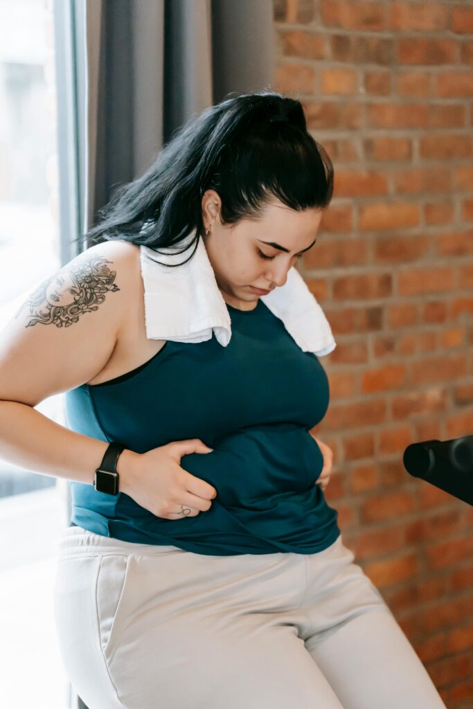 pexels-photo-6551408-6551408 Upset young obese female in sportswear leaning on windowsill and desperately looking at stomach