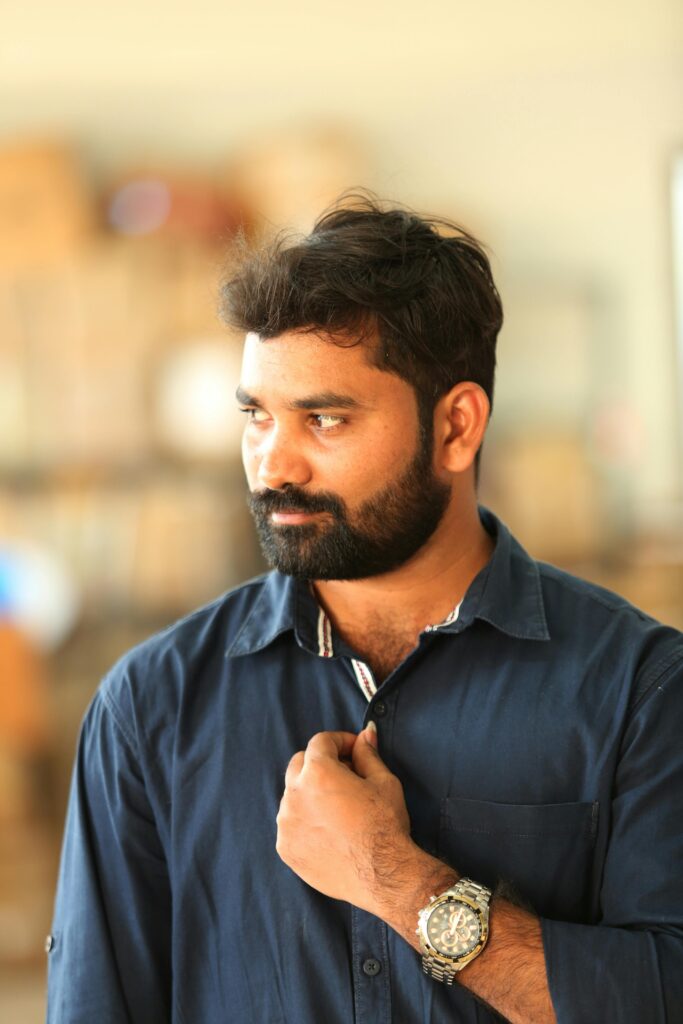 pexels-photo-938639-938639 A thoughtful man with a beard and blue shirt posing indoors, displaying a stylish watch.
